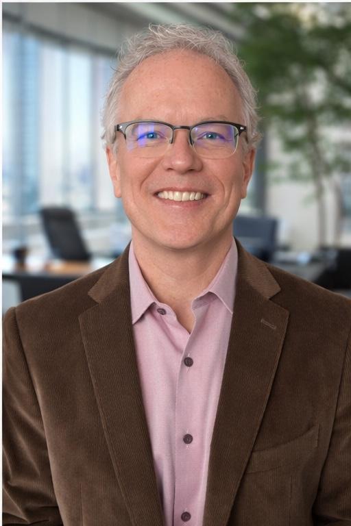 A smiling, gray-haired man wearing a brown suit and glasses.